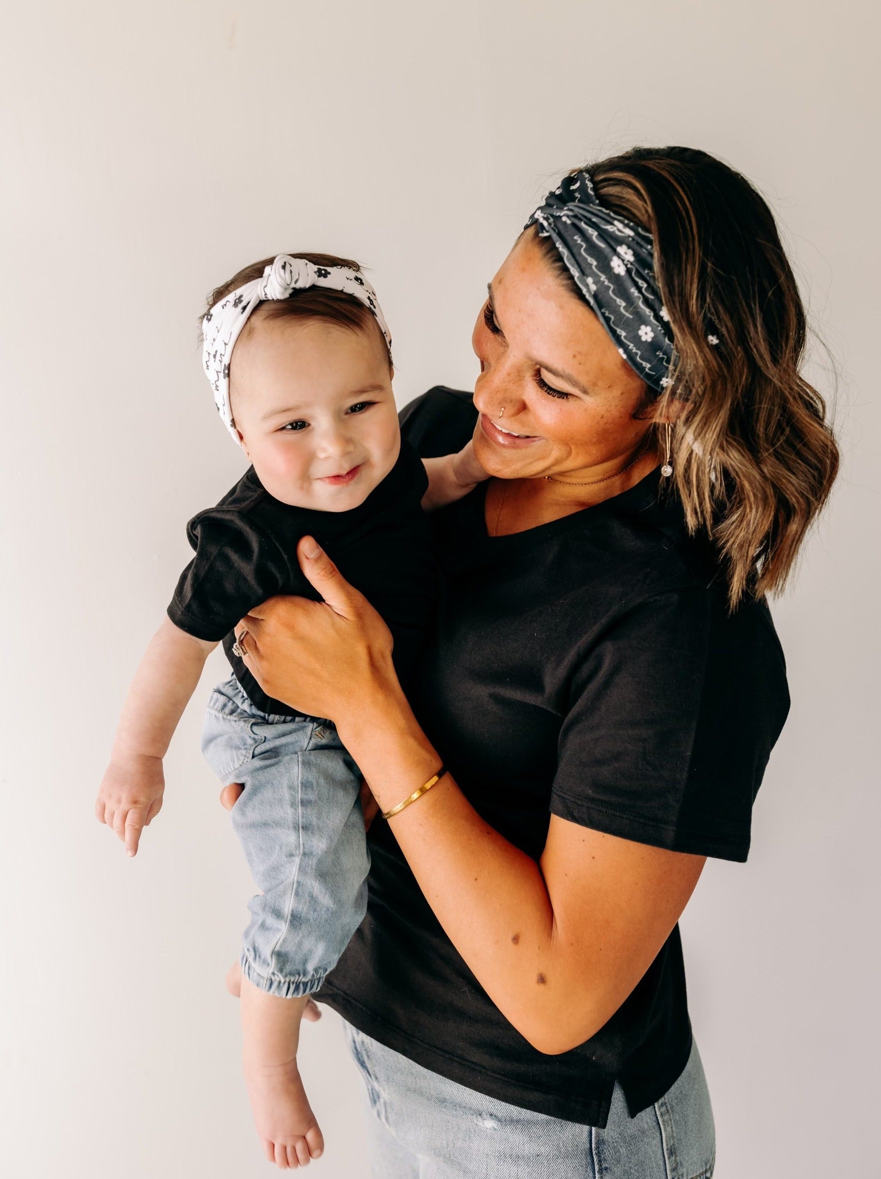 A woman smiles, holding a baby, wearing a twist knot I'm a Cool Mom - Mommy & Me headbands, adjustable for babies and toddlers. Designed in Springfield, MO.