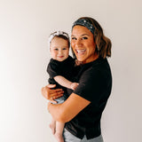 A woman smiles, holding a baby, wearing a twist knot I'm a Cool Mom - Mommy & Me headbands, adjustable for babies and toddlers. Designed in Springfield, MO.