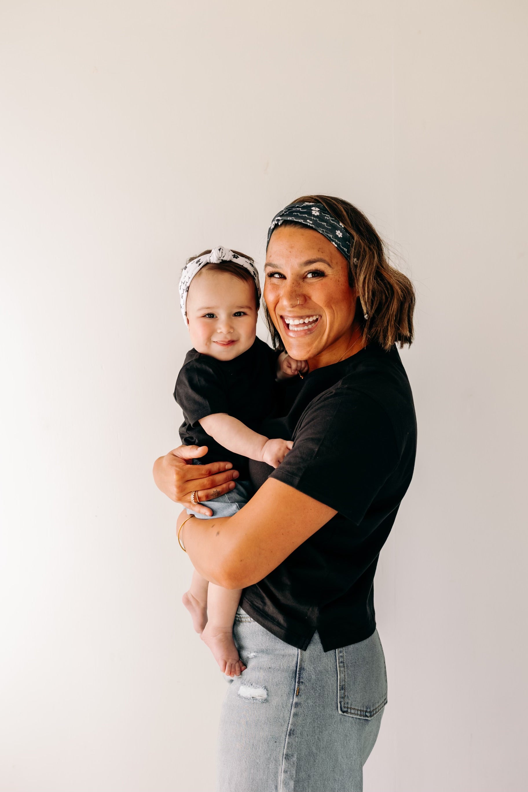 A woman smiles, holding a baby, wearing a twist knot I'm a Cool Mom - Mommy & Me headbands, adjustable for babies and toddlers. Designed in Springfield, MO.