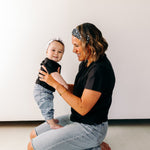 A woman smiles, holding a baby, wearing a twist knot I'm a Cool Mom - Mommy & Me headbands, adjustable for babies and toddlers. Designed in Springfield, MO.
