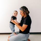 A woman smiles, holding a baby, wearing a twist knot I'm a Cool Mom - Mommy & Me headbands, adjustable for babies and toddlers. Designed in Springfield, MO.