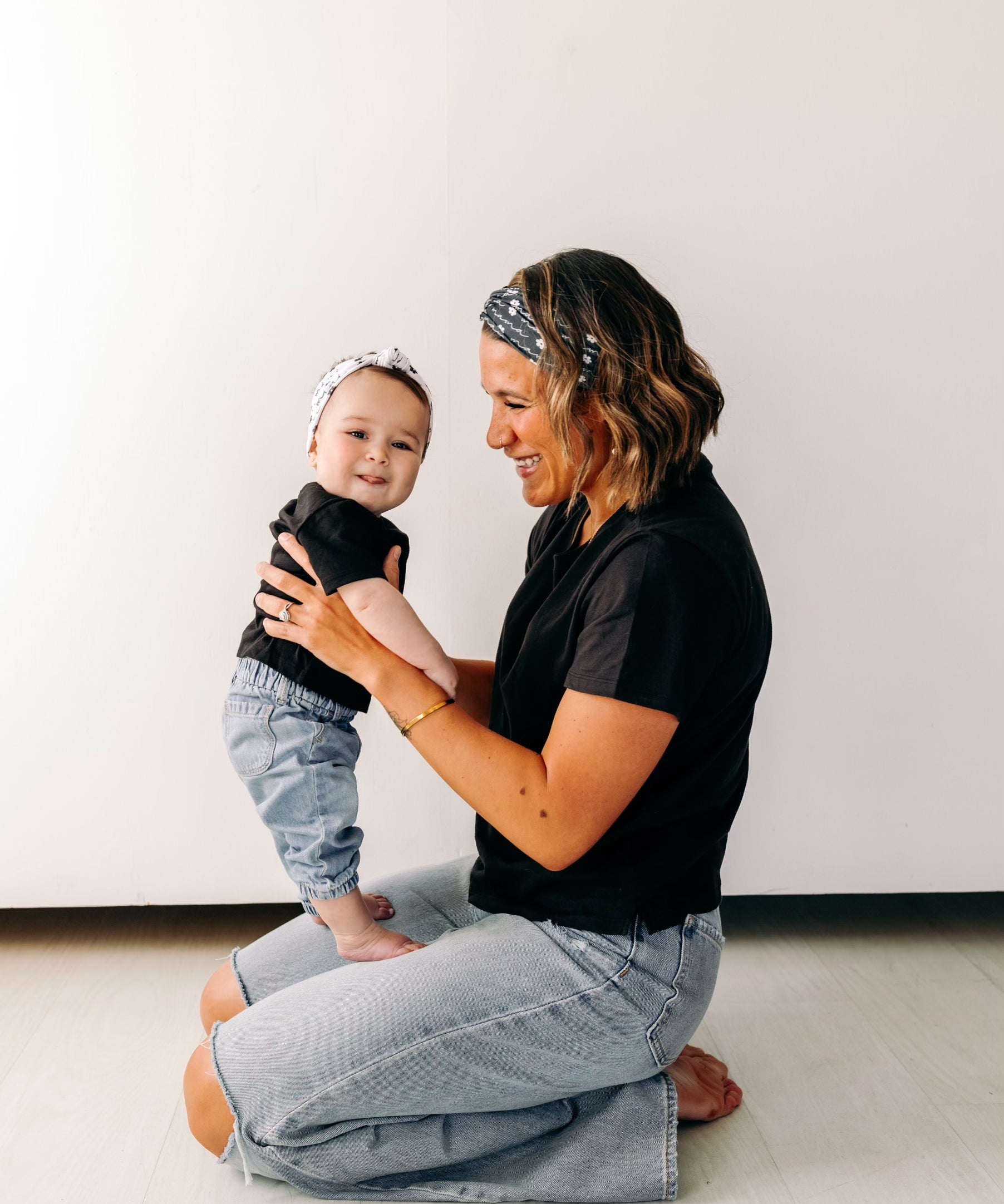 A woman smiles, holding a baby, wearing a twist knot I'm a Cool Mom - Mommy & Me headbands, adjustable for babies and toddlers. Designed in Springfield, MO.