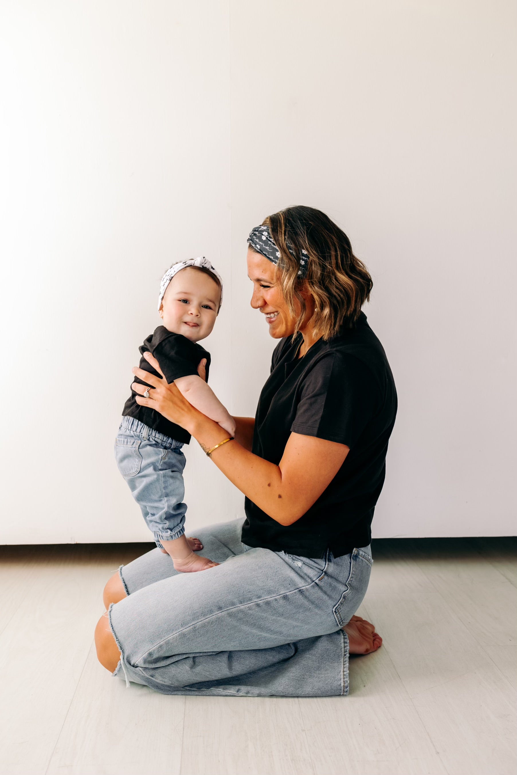 A woman smiles, holding a baby, wearing a twist knot I'm a Cool Mom - Mommy & Me headbands, adjustable for babies and toddlers. Designed in Springfield, MO.
