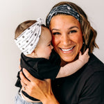 A woman smiles, holding a baby, wearing a twist knot I'm a Cool Mom - Mommy & Me headbands, adjustable for babies and toddlers. Designed in Springfield, MO.