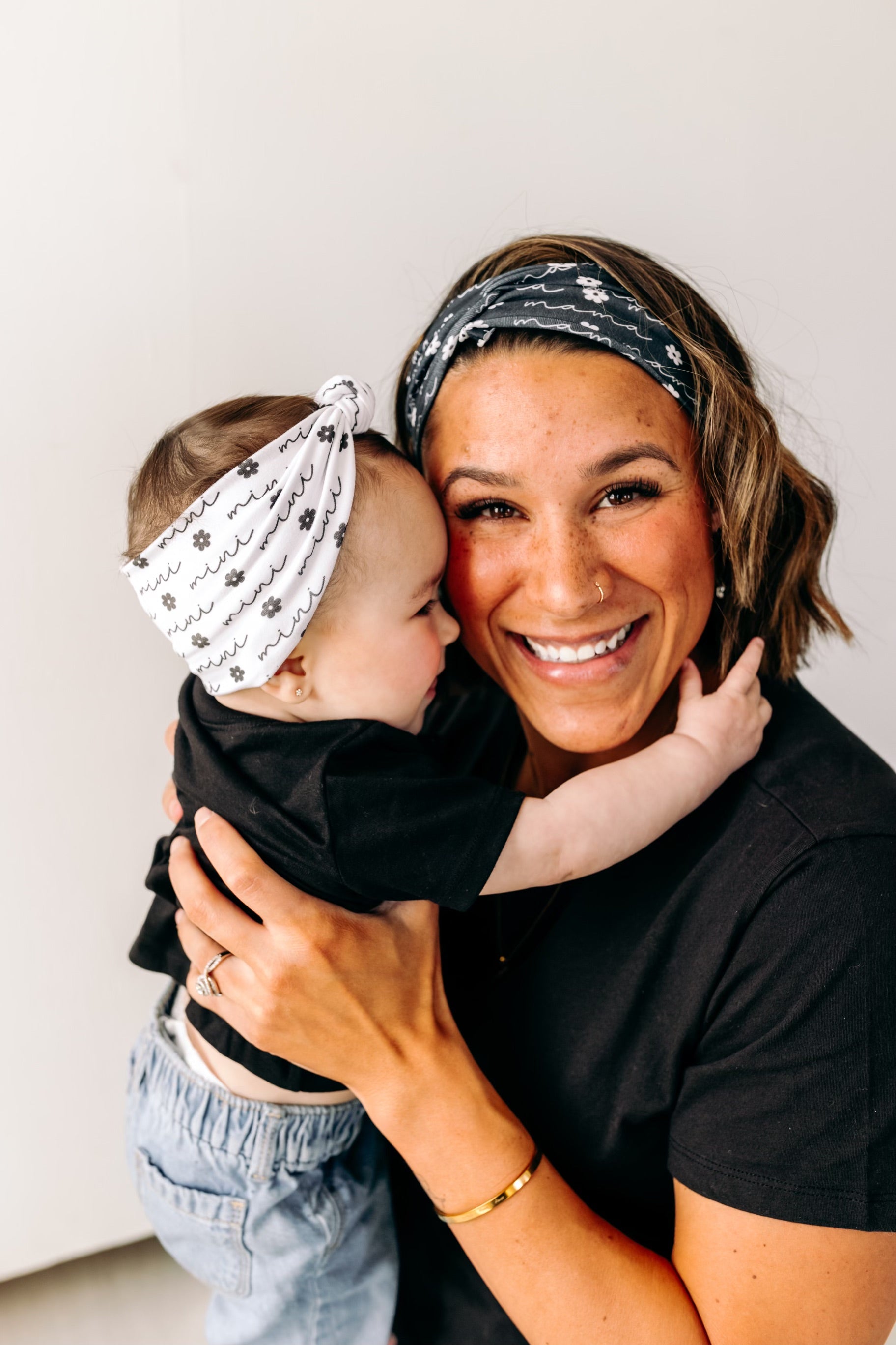 A woman smiles, holding a baby, wearing a twist knot I'm a Cool Mom - Mommy & Me headbands, adjustable for babies and toddlers. Designed in Springfield, MO.