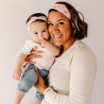A woman smiling, holding a baby, showcasing a twist knot headband set for mommy & me. Adjustable for toddlers and babies, designed in Springfield, MO.