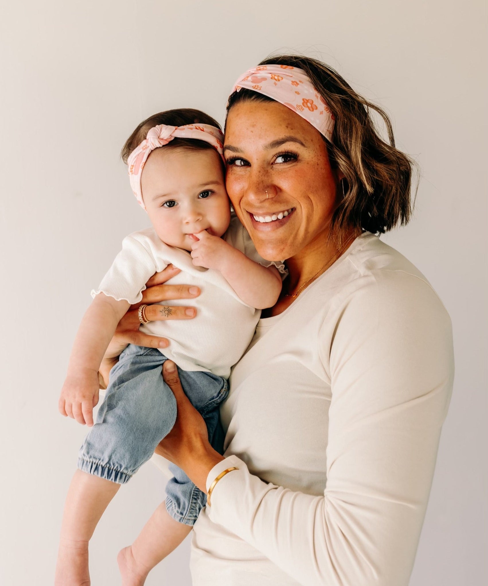 A woman smiling, holding a baby, showcasing a twist knot headband set for mommy & me. Adjustable for toddlers and babies, designed in Springfield, MO.