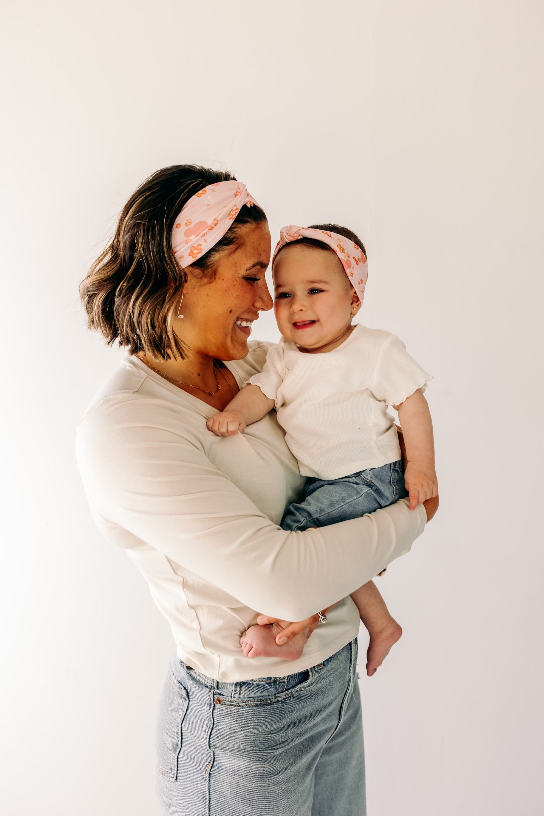 A woman smiling, holding a baby, showcasing a twist knot headband set for mommy & me. Adjustable for toddlers and babies, designed in Springfield, MO.