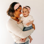 A woman smiling, holding a baby, showcasing a twist knot headband set for mommy & me. Adjustable for toddlers and babies, designed in Springfield, MO.