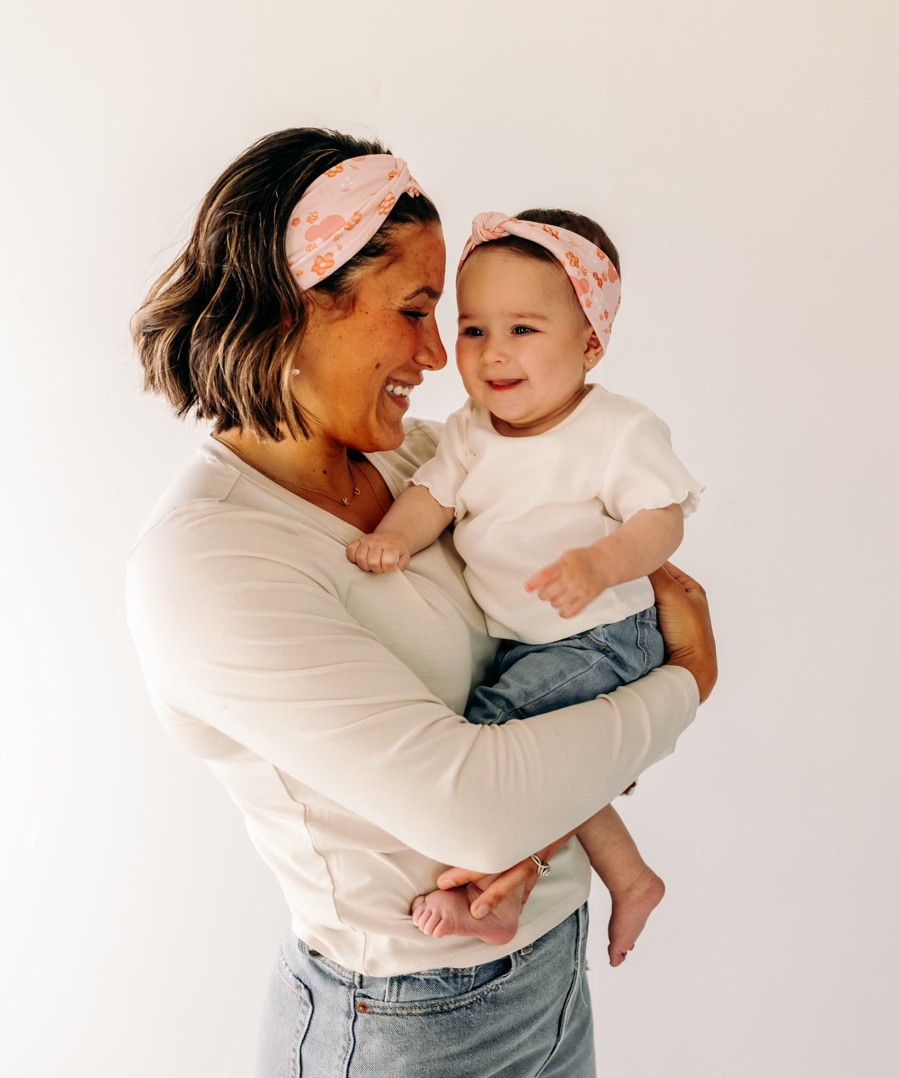 A woman smiling, holding a baby, showcasing a twist knot headband set for mommy & me. Adjustable for toddlers and babies, designed in Springfield, MO.