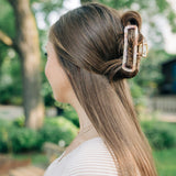 Woman with long hair in a bun, adorned with the Break A Leg Clip from The Sarah Wallace Collection, a marble and metal hair accessory.