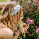 A woman in Lilac Market's Blossom Buddies headband smiles, showcasing its versatile 3-in-1 twist style. Functional, machine washable, and sweat-absorbent for workouts or play.