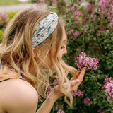 A woman in Lilac Market's Blossom Buddies headband smiles, showcasing its versatile 3-in-1 twist style. Functional, machine washable, and sweat-absorbent for workouts or play.