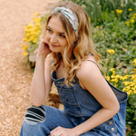 A woman in Lilac Market's Blossom Buddies headband smiles, showcasing its versatile 3-in-1 twist style. Functional, machine washable, and sweat-absorbent for workouts or play.