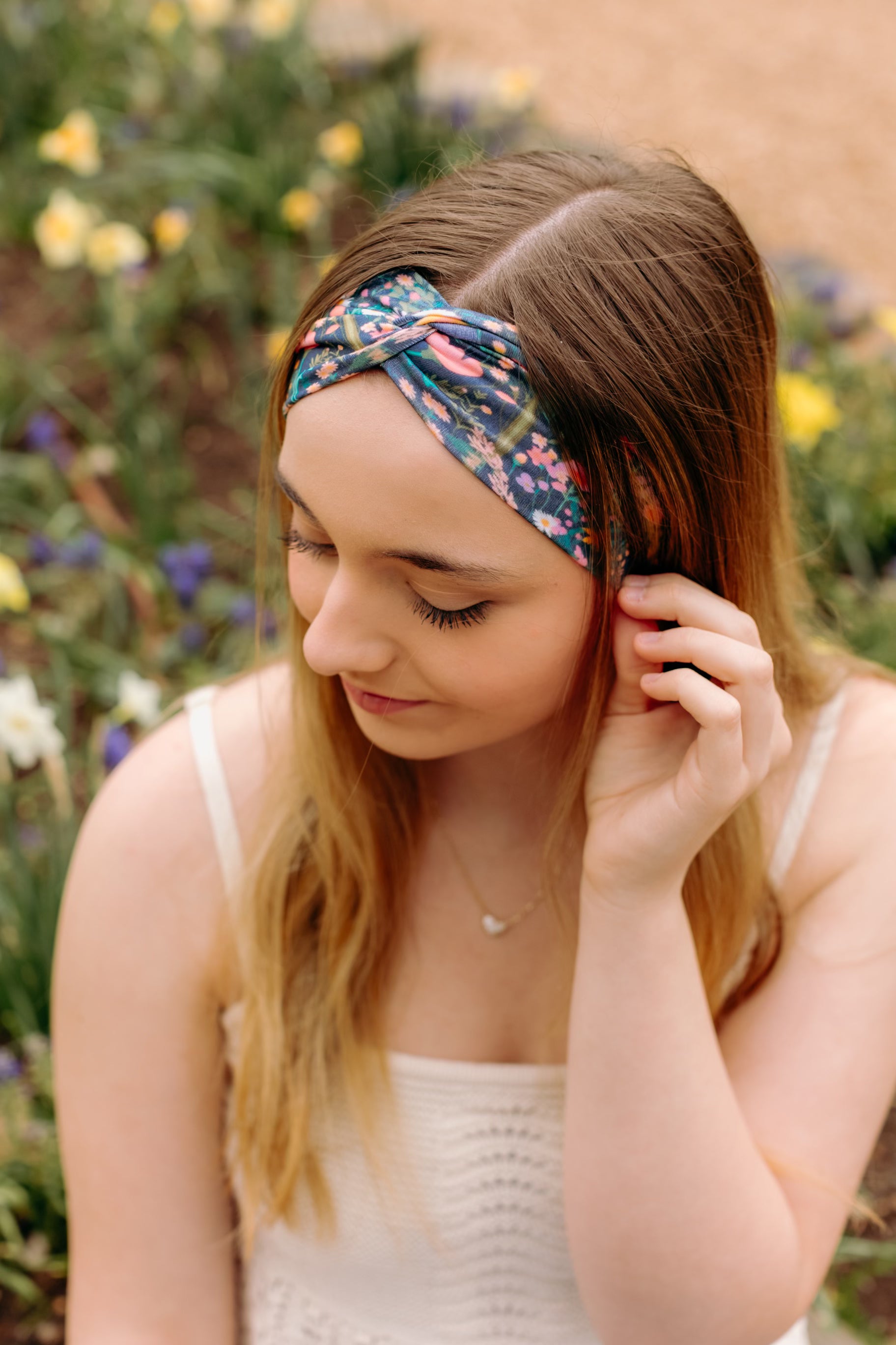 A woman in a Courtney Floral on Navy headband, showcasing a versatile 3-in-1 twist style. Designed for confidence and function, machine washable, sweat-absorbent, and non-slip. Sizes for women and children available.