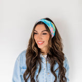Adult women’s headband with allover layered watercolor paint brushstroke print in varying oranges, pinks, yellows, blues, greens and whites.