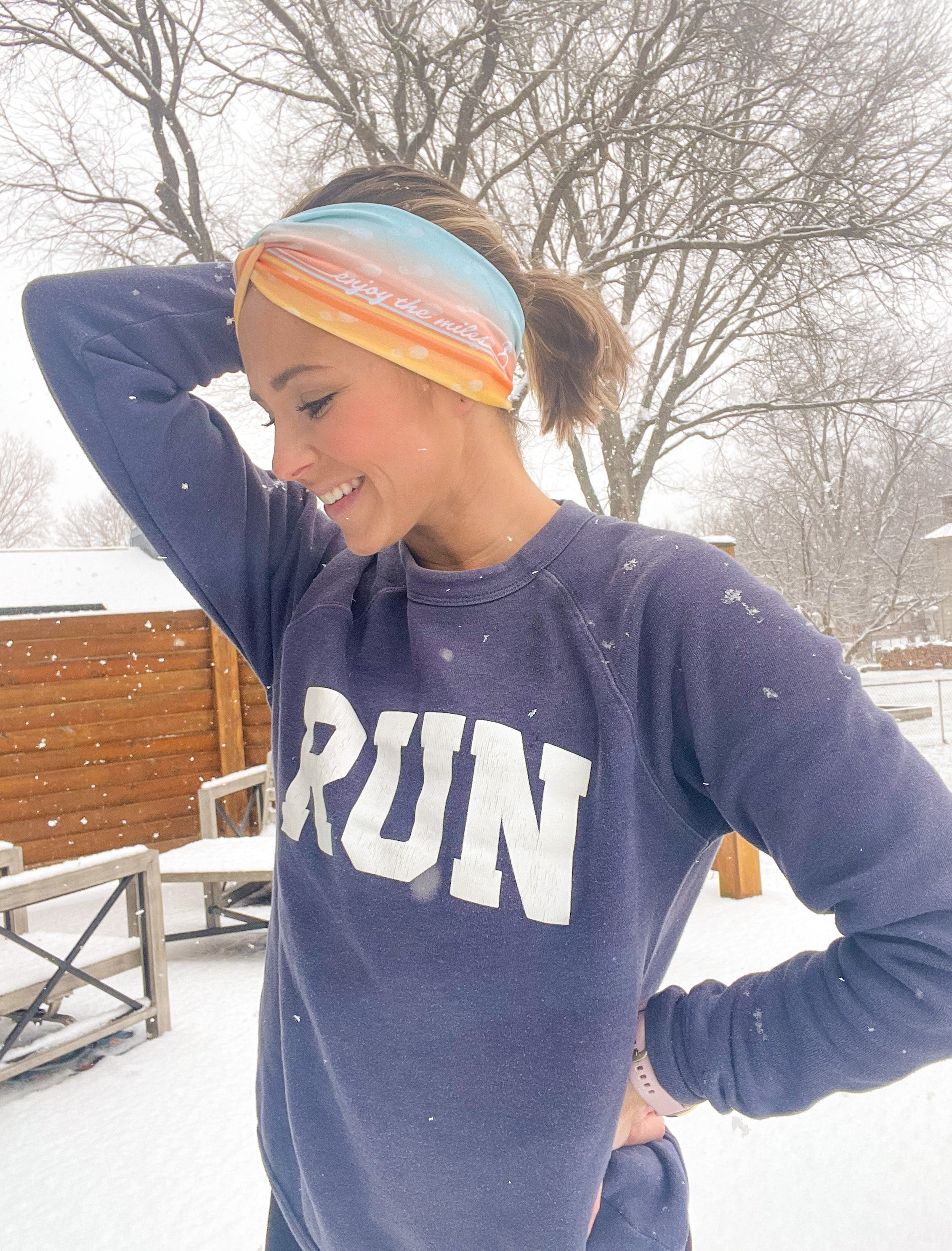 Adult women's gradient headband with yellow, orange and blue with allover white shoe prints, three yellow, orange and white horizontal lines and the white script saying "enjoy the miles"