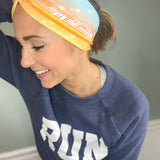 Adult women's gradient headband with yellow, orange and blue with allover white shoe prints, three yellow, orange and white horizontal lines and the white script saying "enjoy the miles"