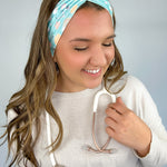 Adult women's blue-teal headband with yellow smiley faces, pink daisies, muted rainbows, and pink stethoscopes with a heart on the end