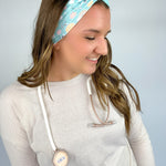 Adult women's blue-teal headband with yellow smiley faces, pink daisies, muted rainbows, and pink stethoscopes with a heart on the end