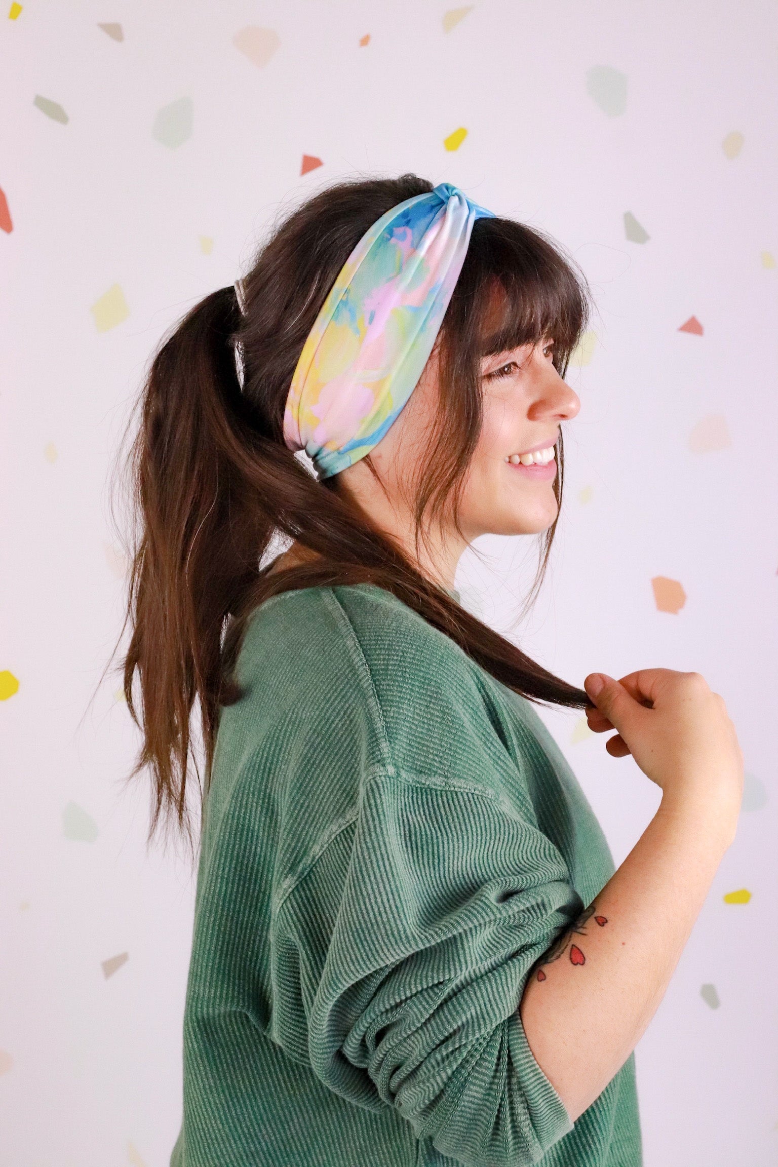 Adult women’s headband with allover layered watercolor paint brushstroke print in varying oranges, pinks, yellows, blues, greens and whites.