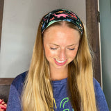 Adult women's black headband with orange, red, blue, grey and pink dinosaur silhouettes with similar colored plants