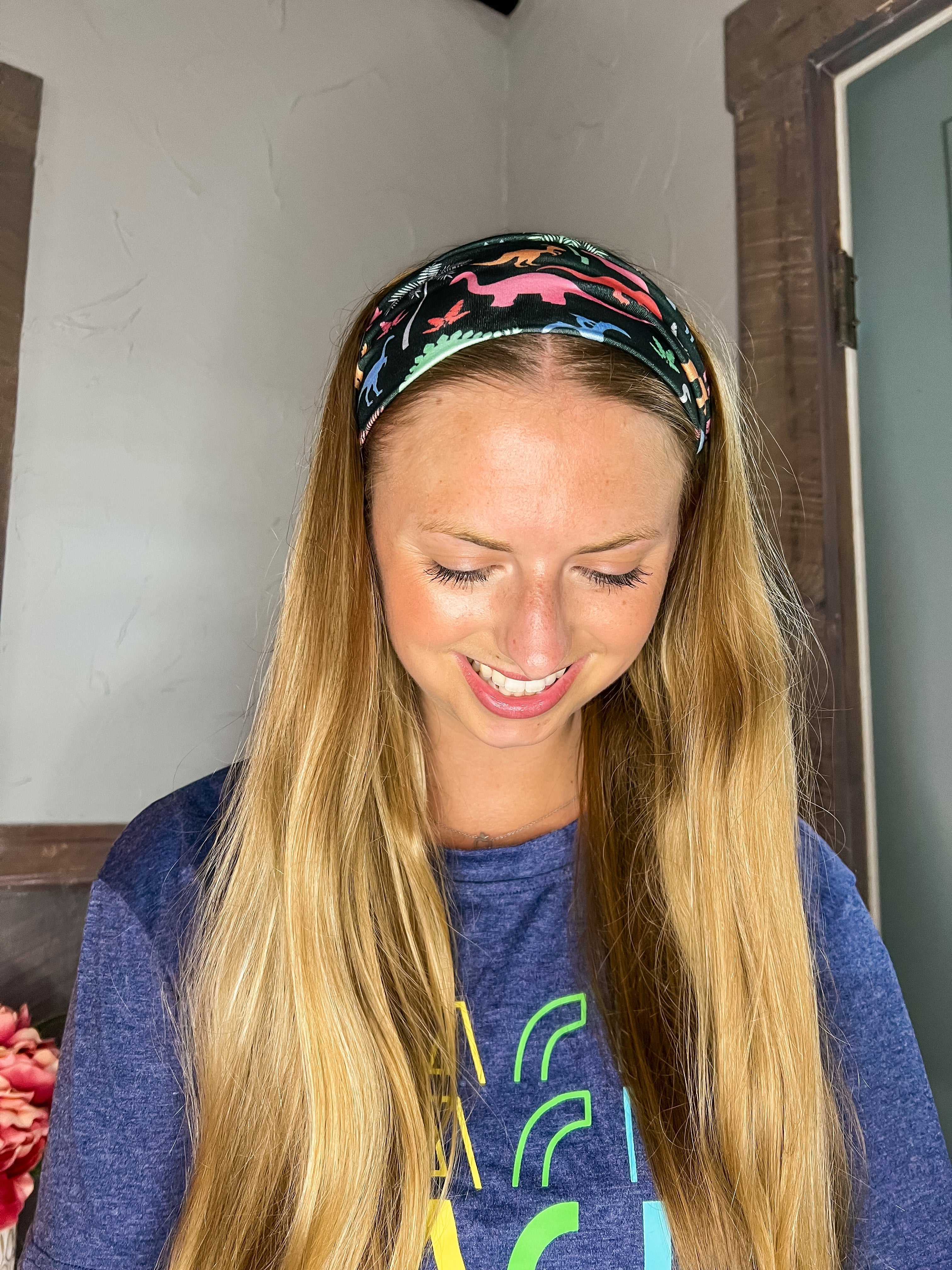 Adult women's black headband with orange, red, blue, grey and pink dinosaur silhouettes with similar colored plants
