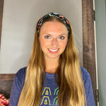 Adult women's black headband with orange, red, blue, grey and pink dinosaur silhouettes with similar colored plants