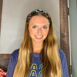 Adult women's black headband with orange, red, blue, grey and pink dinosaur silhouettes with similar colored plants
