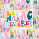 Decorative sticker with 70's style big and small font with the words "Lilac Market" with each letter a different color including orange, pink, teal, green, and blue.