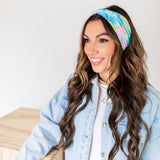 Adult women’s headband with allover layered watercolor paint brushstroke print in varying oranges, pinks, yellows, blues, greens and whites.